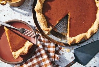 A pumpkin pie with a slice removed on a plate